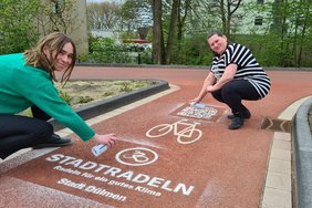 Das Bild zeigt zwei Frauen, die mit Sprühkreide Werbung fürs Stadtradeln auf einen Fahrradweg aufbringen.