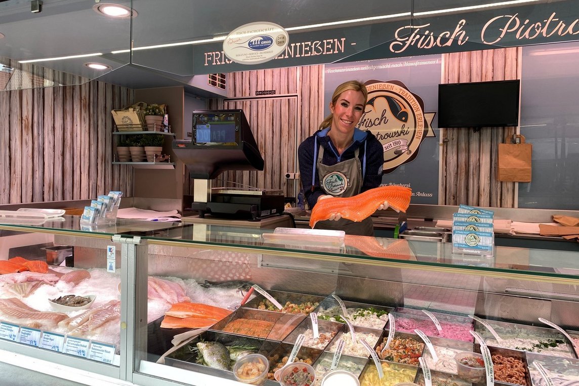 Das Bild zeigt Janet Gahlen mit einem großen Lachfilet in der Hand in ihrem Fischstand.