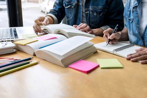 Zwei Personen arbeiten an einem Tisch mit Büchern und Laptop