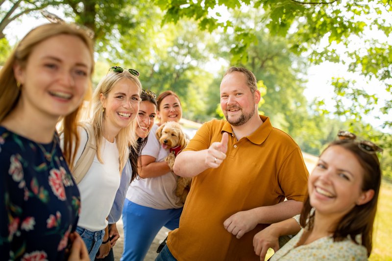 Ihre Vorteile Mitarbeitende stehen in einer Gruppe und lachen. Einer zeigt "Daumen hoch".