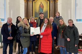 Ann-Kathrin Bruns, Leiterin des städtischen Fachbereichs Bauaufsicht und Denkmalschutz, überreicht die Denkmalplakette an Bauherrin und Eigentümerin Britta Markert-Löbbert. Mit ihnen freuen sich Roland Markert und Kirsten Apke-Lobmeyer von der Stadt Dülmen. Auch Vertreterinnen und Vertreter des Architekturbüros Spital-Frenking + Schwarz sowie der beteiligten Betriebe waren zur Übergabe der Denkmalplakette gekommen.