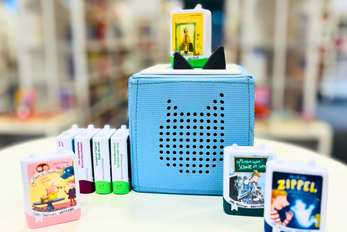 Auf dem Foto sieht man eine hellblaue Toniebox um die verschiedene Book Tonie-Figuren aufgestellt wurden.
