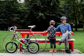 Das Foto zeigt Vater und Sohn auf einer Parkbank, daneben stehen zwei Fahrräder.