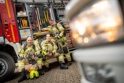 Mitarbeitende der Feuerwehr stehen vor einem Feuerwehrfahrzeug.