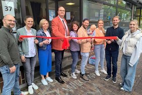 Das Foto zeigt Sozialdezernent Christoph Noelke, der gemeinsam mit Mitarbeitenden des Fachbereichs Jugend und Familie das rote Band durchschneidet. 