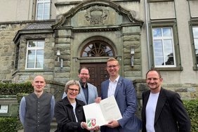 Vor der Hermann-Leeser-Schule: Kirsten Apke-Lobmeyer vom städtischen Fachbereich Bauaufsicht und Denkmalschutz überreicht im Namen des Landes NRW die Denkmalplakette nebst Urkunde an Bürgermeister Carsten Hövekamp. Auch Stadtbaurat Markus Mönter (Mitte), Stadtarchivar Dr. Stefan Sudmann (li.) und Robert Schneider, Leiter der Hermann-Leeser-Schule, freuen sich über die Auszeichnung.  Foto: Stadt Dülmen/Kannacher